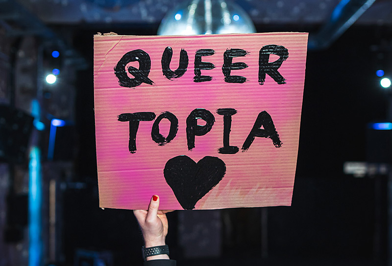 Hand haelt Schild mit der Aufschrift Queer Topia hoch