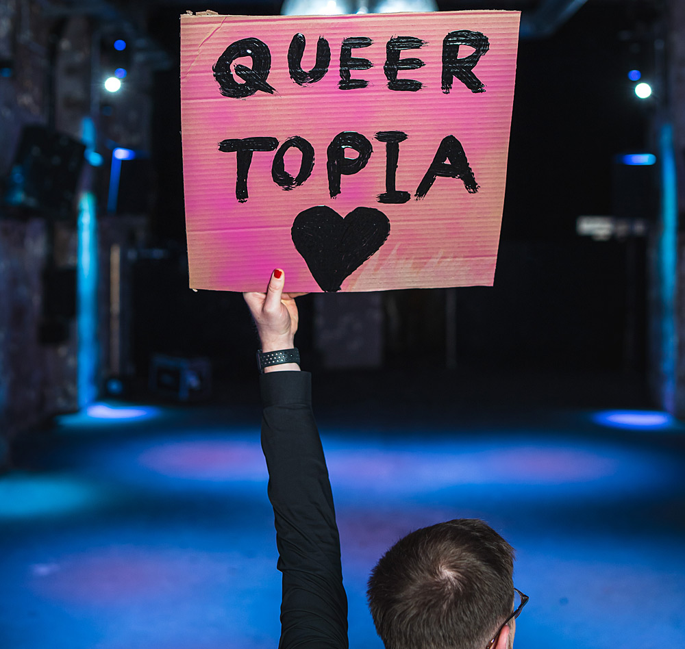 Person haelt Schild mit der Aufschrift Queer Topia hoch