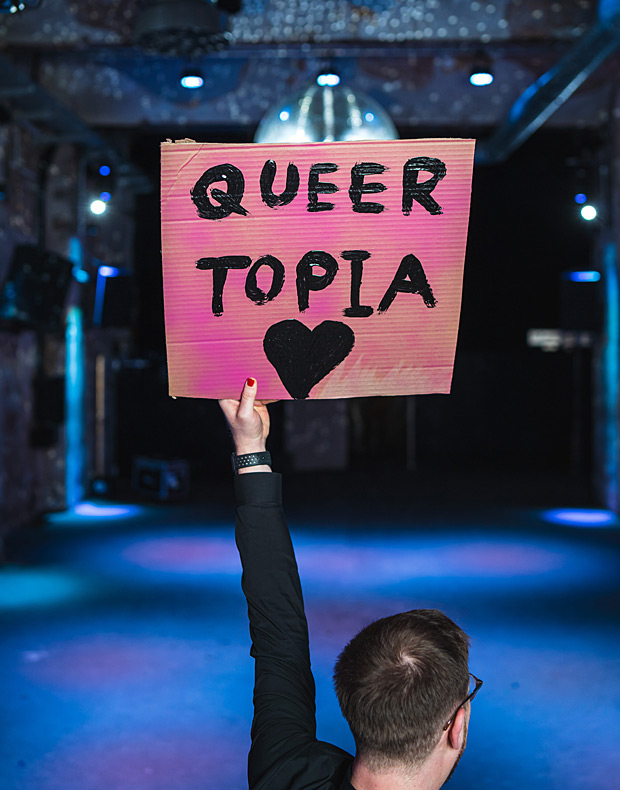 Hand haelt Schild mit der Aufschrift Queer Topia hoch